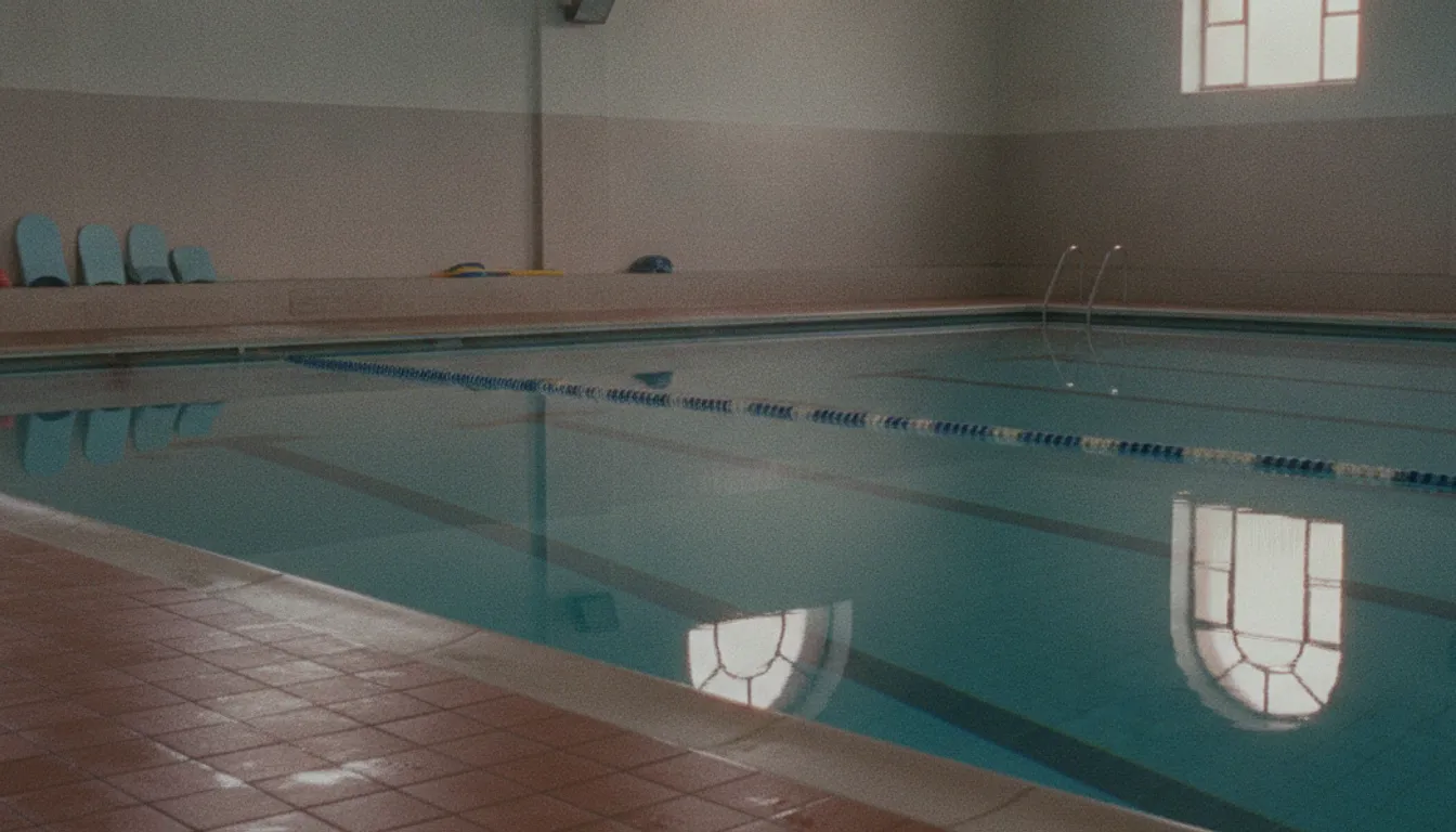 An empty lane at an indoor swimming pool early in the morning, the water still and the tiled edge in the foreground.